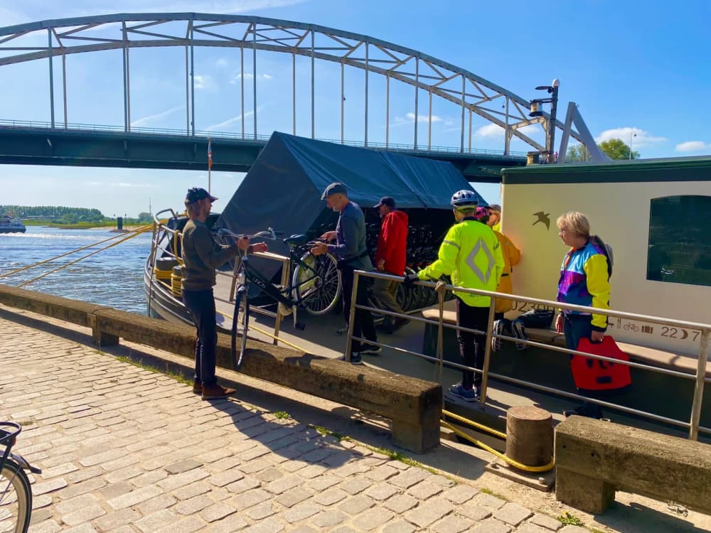 Guests in cycling jackets bringing their bikes on board Ship Josefien beneath a river bridge